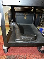 Metal horse statue laying on a black metal cart shelf, dark finish, stylized design.