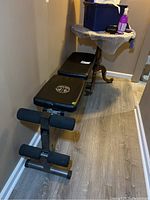 Full view of black Jack LaLanne weight bench showing padded seat and leg foam rollers beside a table.