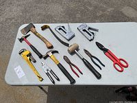 Full view of all hand tools on white table showing a variety of hammers, wrenches, pliers, staplers, and scissors
