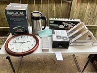 Overview of the household item lot showing all items on table including Magical Butter box, wall clock, knife sharpener, glove, flatware box and knife block.
