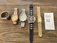 Five wristwatches laid out on wood surface showing variety in band styles including metal and rubber.