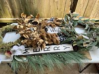 Overview photo showing five decorative wreaths laid out, along with a wooden 'WELCOME' sign with black text on white background.