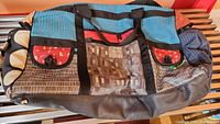 Front view of the large multicolor patchwork duffle bag with black handles and front pockets.