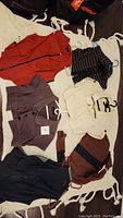 Top-down photo showing all six clothing items on a white textured blanket, including vests, sweaters, and a jacket in various colors and patterns.