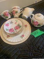 Porcelain tea set pieces showing cups, saucers, plates, creamer, and sugar bowl with rose floral pattern and gold trim.