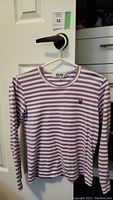 Front view of the Comme Des Garcons Play long sleeve shirt on hanger. White and purple horizontal stripes, red heart logo visible on left chest.