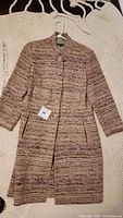 Front view of women's tweed jacket laid flat on cream knit surface.