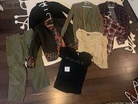Image showing seven clothing items including pants, jackets, shirts, and t-shirts arranged on floor.