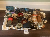 Full view of 27 belts of different colors, materials, and buckle styles laid on a white cloth with a tag number 10.