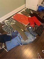 Photo showing the full assortment of pants including camouflage, colored, and denim pairs laid out on the floor.