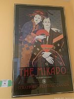 Framed poster featuring two characters in traditional attire holding a red fan with text The Mikado by Gilbert & Sullivan, Stratford Festival Canada June to August 1982.