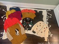 Full lot of nine women's sweaters and cardigans arranged on a white woven mat on dark hardwood floor.