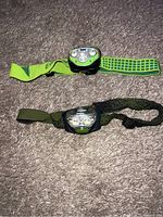 Two headlamps on carpet, one bright green strap with Energizer branding, the other black and green strap with grid pattern