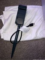 Front angle of green outdoor plug-in timer resting on white cloth, showing ground stake and power cord with plug.