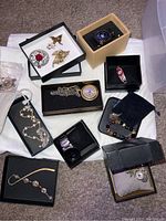Various boxed jewelry pieces including pocket watches, brooches, pins, bracelets, and necklaces arranged on carpet.