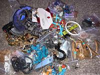 Photo of assorted Indian style jewelry showing turquoise stone necklaces, chains, feathers, rope and bead elements scattered on carpet, packaged in small clear bags.