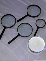 Top-view photo showing five magnifying glasses arranged on a flat surface, four with black handles and one with a silver rim.