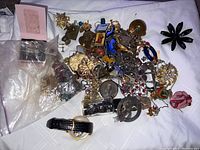 Overview of assorted jewelry including brooches, pins, watches, chains, and small decorative items on white cloth.