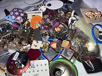 Top view of a heap of assorted costume jewelry showing multiple pairs of earrings, bracelets, pendants, and other pieces including bellybutton rings in various colors and materials.