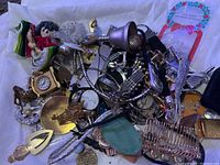 Photo showing assorted unsearched jewelry items, pins, brooches, coins, pens, and small collectibles in a pile.