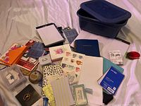 Full view of assorted office and school supplies spread out including cards, notepads, ink stamp, tape dispenser, and storage containers.