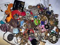 A dense assortment of mixed costume jewelry pieces piled together including rings, bracelets, earrings, and necklaces in copper, gold, and silver tones with colorful accents.