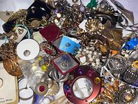 Overhead view of a varied pile of costume jewelry including earrings, brooches, and pendants with colorful stones and metallic finishes.