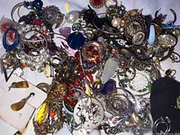 A large pile of assorted jewelry including earrings, bracelets, necklaces with mixed colors and materials like gold-tone and silver metals, stones, and crystals.