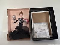 Full view of Barbie doll in box with lid removed, showing doll in gown with accessories and paperwork.