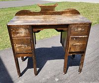 Full view of antique wooden dressing table showing front with six drawers and curved backboard, outdoors on pavement.