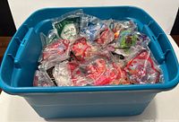 Blue bin filled with multiple sealed McDonald Happy Meal toys in original plastic packaging, showing a variety of licensed character toys.