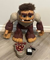 Front view of Fisher Price Imaginext Bigfoot monster toy, remote control with six buttons, and battery pack.