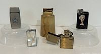 Five vintage lighters arranged on clear plastic bases, featuring various styles and materials including mother of pearl and metal.