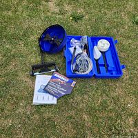 Photo showing all Simoniz power washer accessories laid out on grass including blue floor scrubber drum, hoses, brush heads, connectors, and manuals.