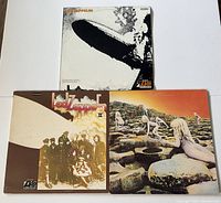 Three Led Zeppelin vinyl records with their covers laid out showing front covers of Led Zeppelin I, Led Zeppelin II, and Houses of the Holy.