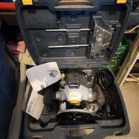 Image of the open plastic carrying case containing the Mastercraft plunge router, instruction manuals, and metal guide accessory.