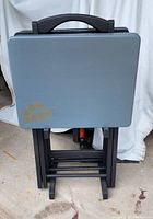 Set of 4 TV trays stacked on black wooden stand, showing grey/blue tops with gold leaf accents and black legs.