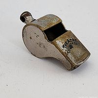Side view of vintage brass police whistle showing patina and 'The Acme Thunderer' marking