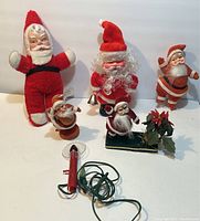 Photo of the complete lot showing five vintage Santa Claus dolls and a red electrical wired component, arranged against a white background.