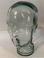 Front side view of the clear glass mannequin head with green tint, showing facial features and smooth contours.