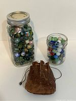 Front view of two Mason jars filled with marbles and the leather drawstring pouch in front.
