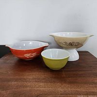 Three vintage Pyrex mixing bowls side by side on wood surface: Wheat Autumn, Homestead, and Primary Color.