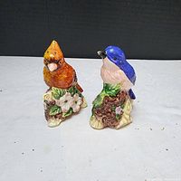 Front angled view of vintage ceramic cardinal and blue jay salt and pepper shakers on white surface with black background