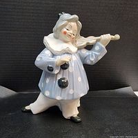 Front view of porcelain clown figurine dressed in blue polka dot outfit playing violin.