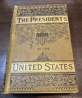Front cover of hardcover book showing yellow cloth binding with black and gilt stamped design and title 'The Presidents of the United States Illustrated'