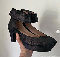 Photo showing right side and front view of a single black platform pump with ankle strap held in hand, against a plain background.