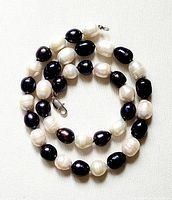 Coiled view of the black and white natural pearl necklace showing the alternating black and white pearls and metal clasp.