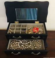 Full view of open black jewelry box showing upper compartment and drawer with jewelry.