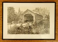 Framed black and white etching displayed on a wooden surface showing Fieldville covered bridge.