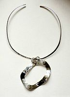 Full view of pendant and flat hard wire necklace on white fabric background, showing shape and design of both items.